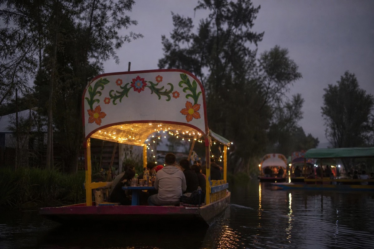 Festive trajinera party boat with string lights and drinks on the Xochimilco canals at dusk