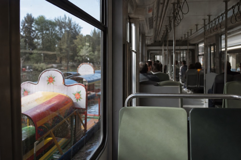 A light-rail carriage interior with hanging straps and daylight coming through the windows