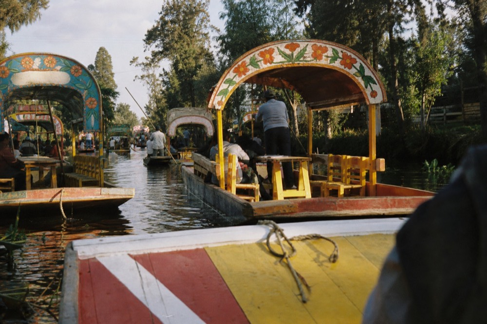 Narrow canal channel packed with heavy wooden boats passing within centimetres of each other, poles pushing off the banks