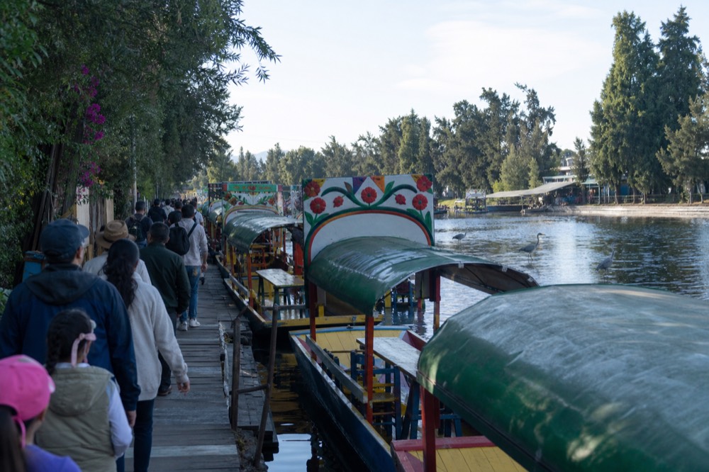A crowded dock walkway on a weekend with families queueing beside moored canopied boats