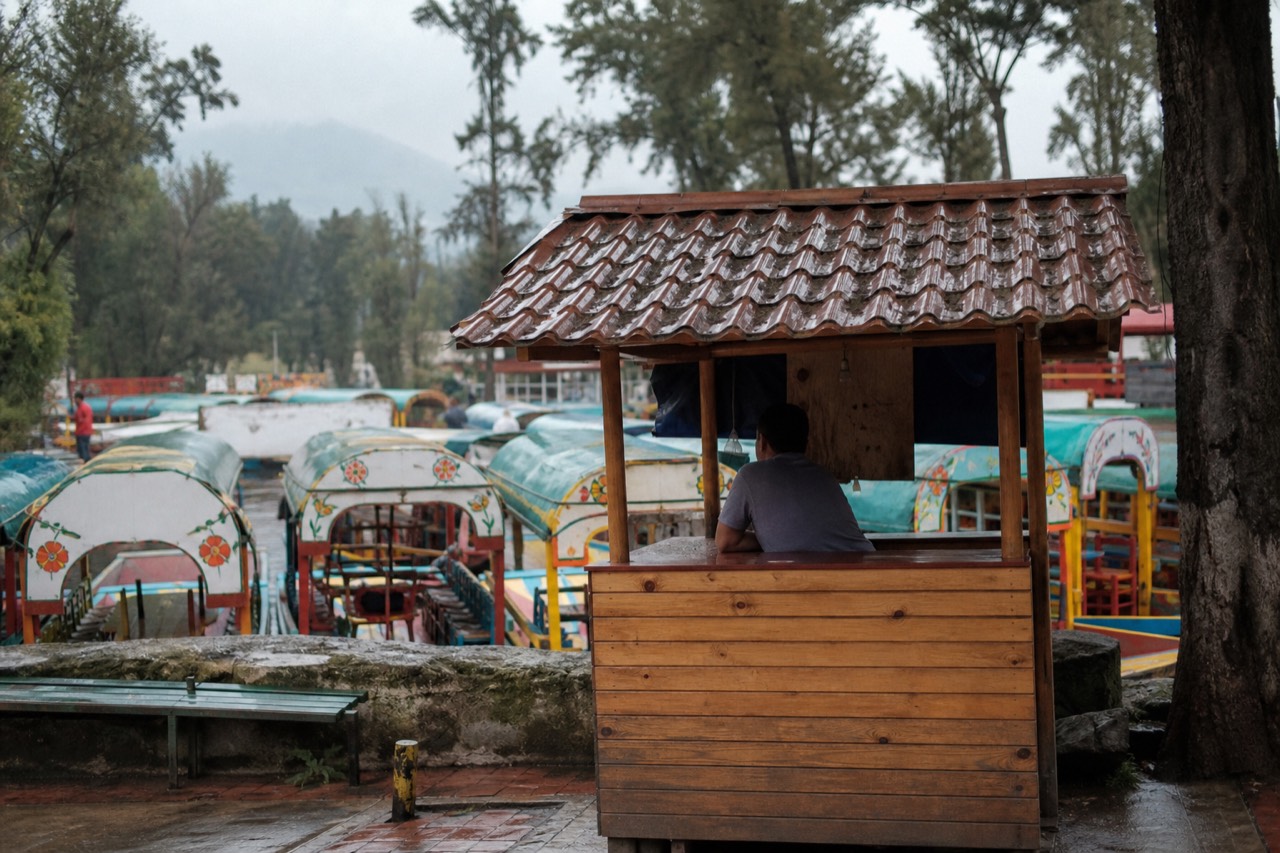 A wooden ticket kiosk at the entrance to a busy canal dock with rows of canopied boats waiting behind it