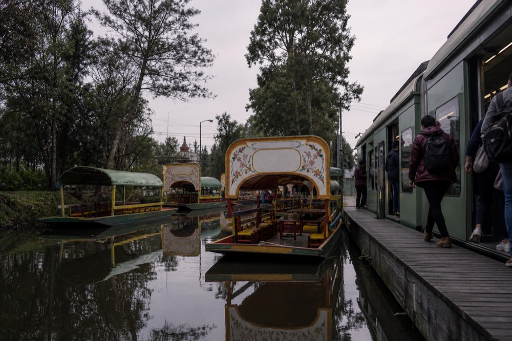A light-rail train waiting at an open-air platform with passengers stepping aboard in soft morning light