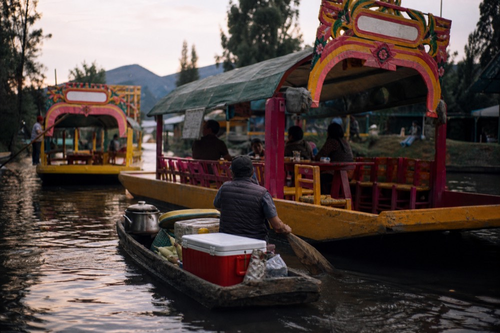 A small paddled canoe loaded with an ice chest and a corn pot pulling alongside a larger flat-bottomed canal boat
