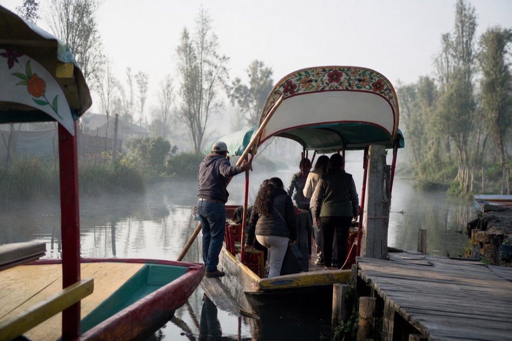 A poler steadying a canopied boat against a wooden dock while passengers step aboard one at a time