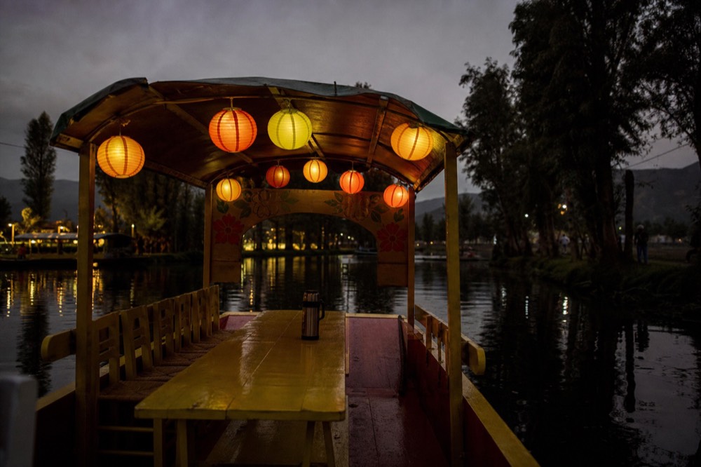 Paper lanterns strung along the canopy of a moored canal boat at night, empty benches and a thermos on the table inside