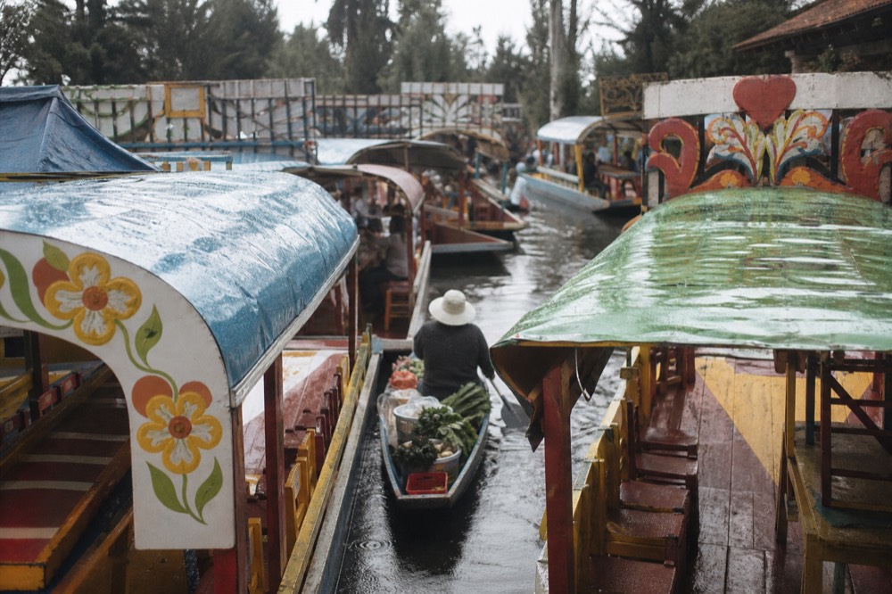 Crowded midday canal scene with a dozen colourful roofed boats packed side by side and a small vendor canoe squeezing between them