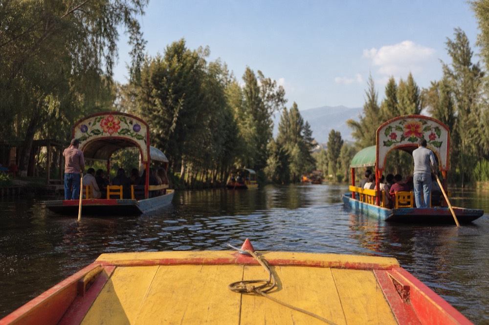 Wide canal seen from the bow of a moving flat-bottomed boat, two other canopied boats passing in opposite directions under a bright midday sky
