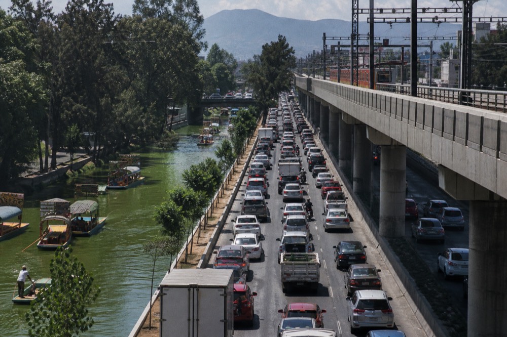 Wide view of a broad Mexico City avenue at rush hour with dense traffic under an elevated rail line, seen from a pedestrian bridge