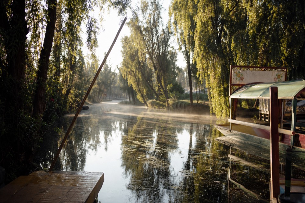 Empty canal at first light with mist over the water and a single boat pole leaning against a wooden landing, no people in sight