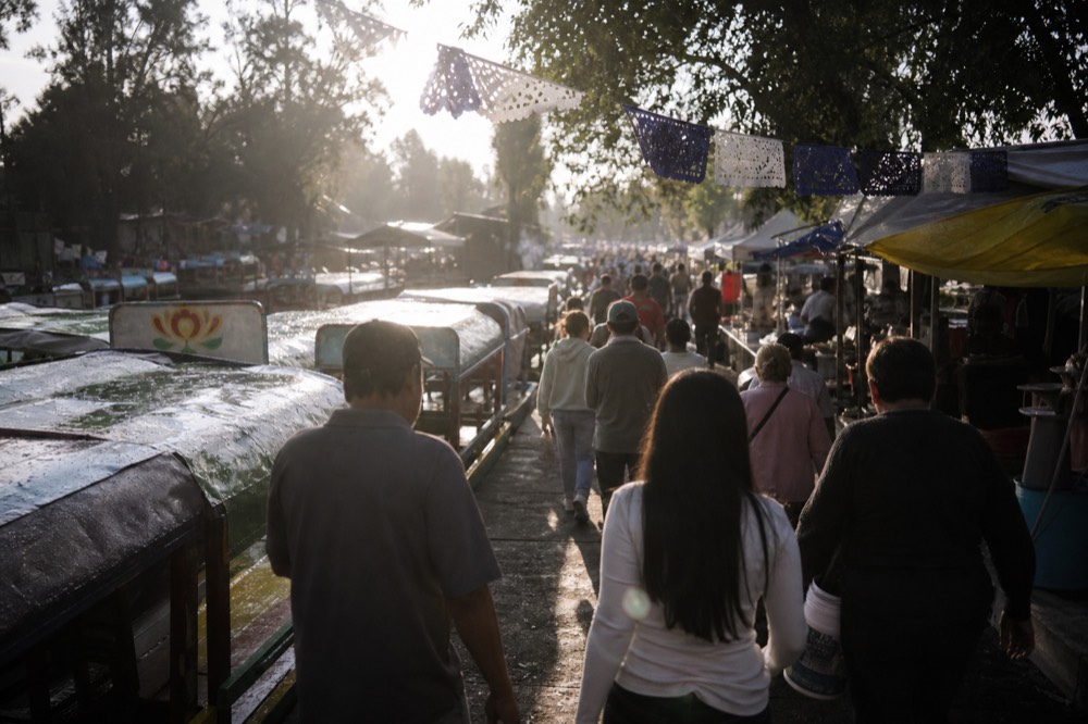 Late afternoon crowd streaming away from a canal dock past food stalls, long shadows and strings of paper flags overhead