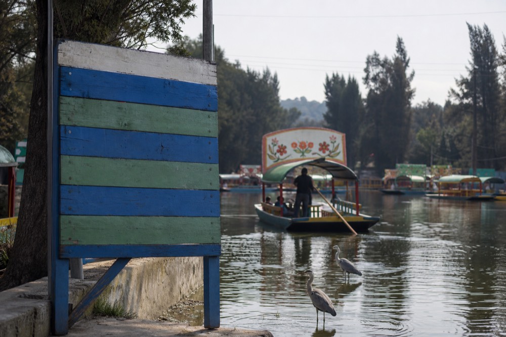 Painted wooden board at a canal landing listing hourly boat rates in pesos, weathered by sun and rain