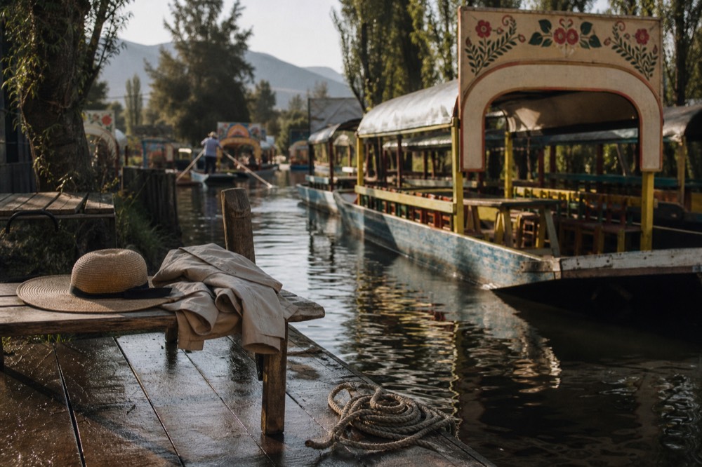 Wet wooden dock boards with a coiled mooring rope, sun hats and a light jacket left folded on a bench beside moored boats
