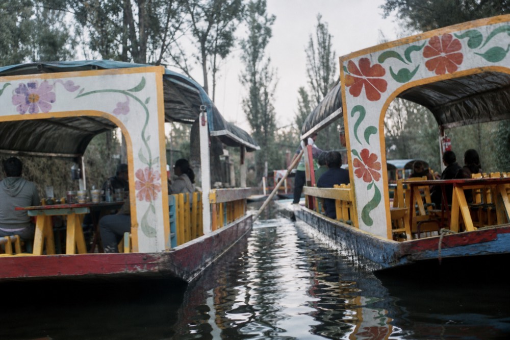 Two canopied canal boats nudging past each other in a narrow channel, painted arches almost touching, reflections breaking in dark green water