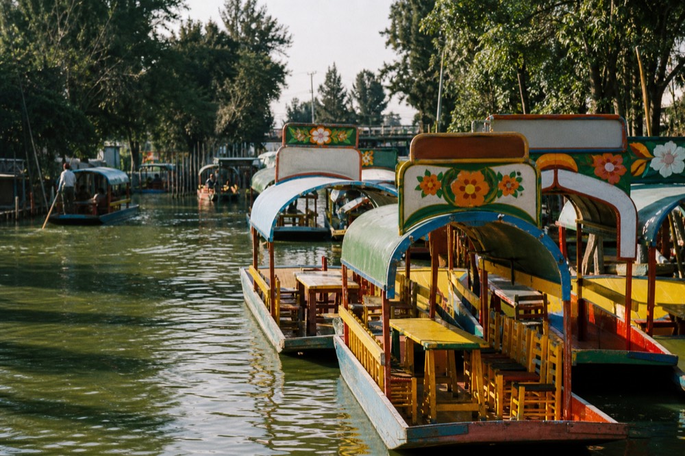 Late afternoon on the water with long shadows across a wide canal and a cluster of moored boats tied together side by side