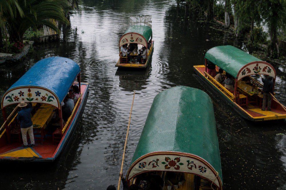 Overhead view of a wide canal junction where four canopied boats converge from different channels, ripples crossing between them