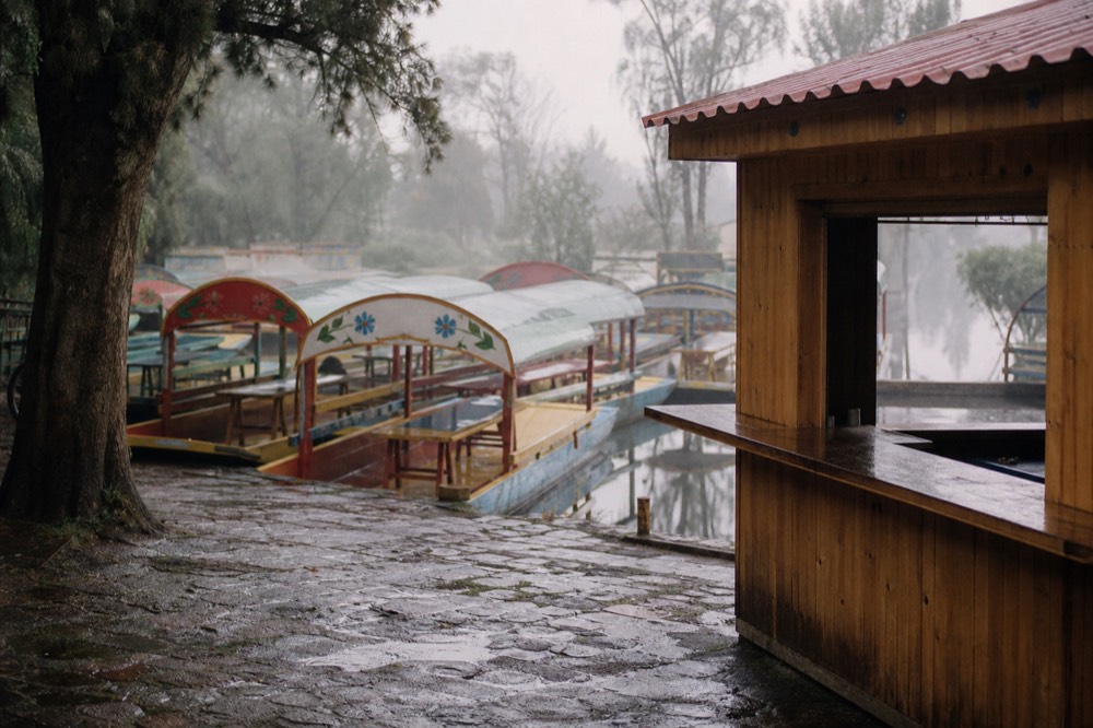 Early morning at a quiet ecological-park boat landing, mist over the water, empty moored boats and a wooden ticket kiosk