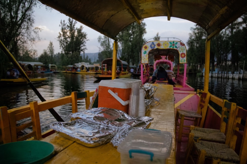 Cooler box, foil-wrapped food trays and a stack of plastic cups arranged on the long wooden table running down the middle of a canal boat